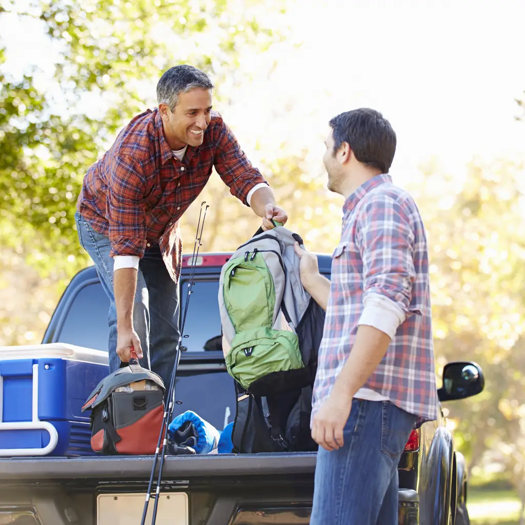 Two campers handle bags and a cooler in a pickup bed.