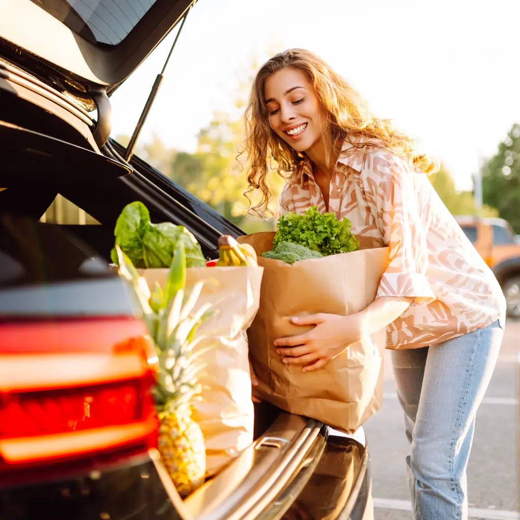 A woman loading groceries through an open vehicle hatch.