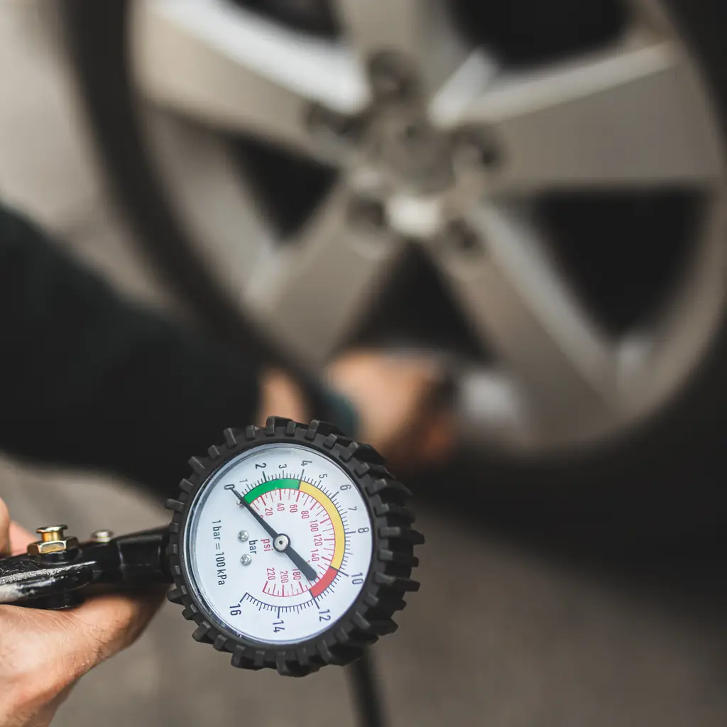 A tire-pressure gauge held beside a vehicle wheel.