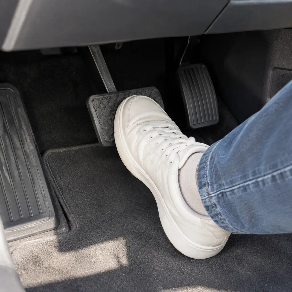 Close view of a parked car footwell with the driver foot resting on the brake pedal