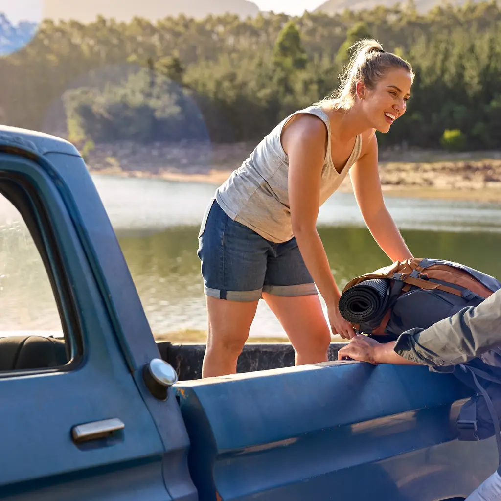 Two people unloading camping gear from a pickup beside a lake.