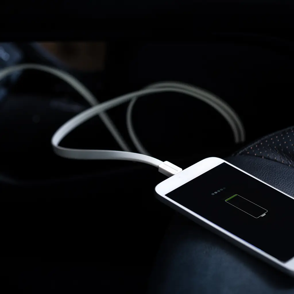 A mobile phone connected to a charging cable on a vehicle seat.