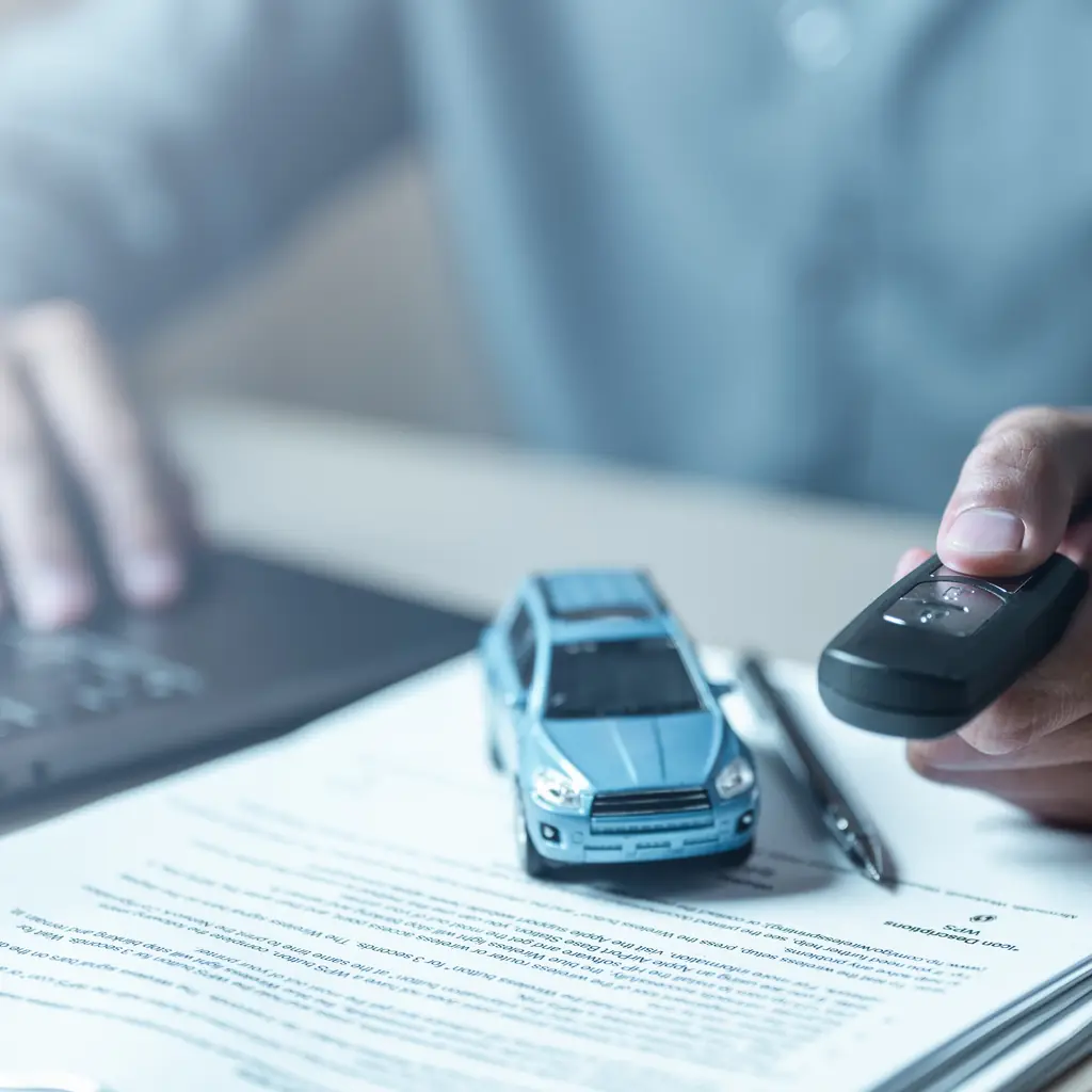 A vehicle key, paperwork, laptop and small model car on a desk.