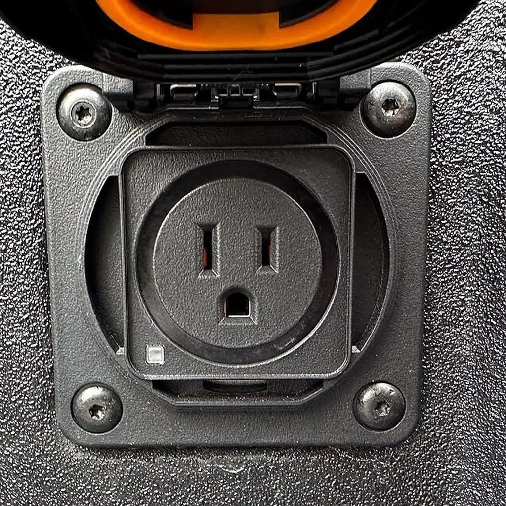 A covered AC power outlet in the bed of a GMC Sierra pickup.