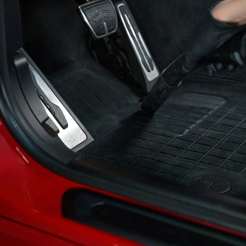 A vacuum nozzle cleaning a vehicle footwell mat.