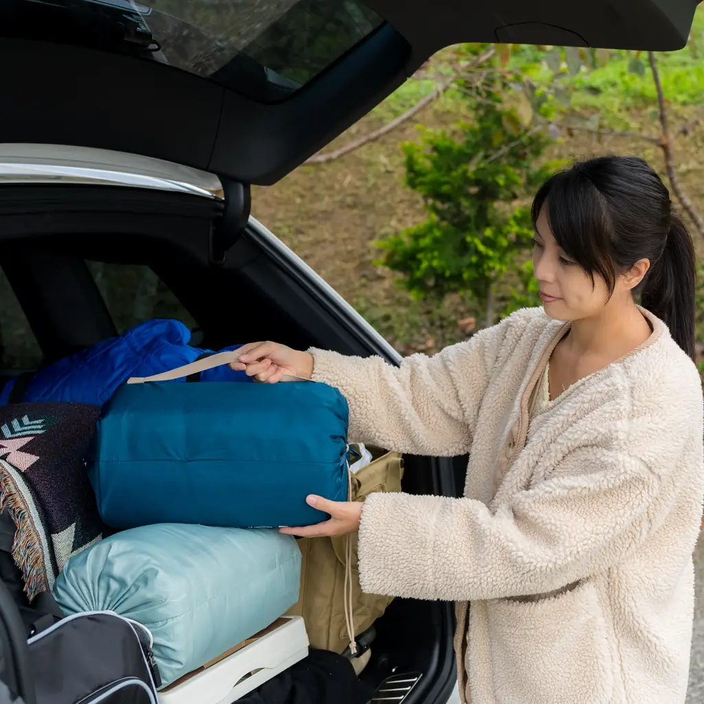 A woman retrieves a soft camping bag from a loaded vehicle.