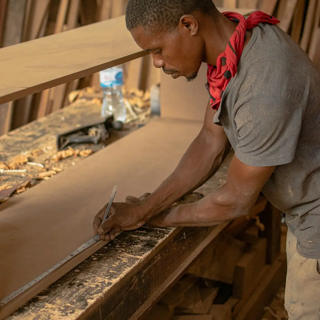 A carpenter measuring a wooden board in a workshop.