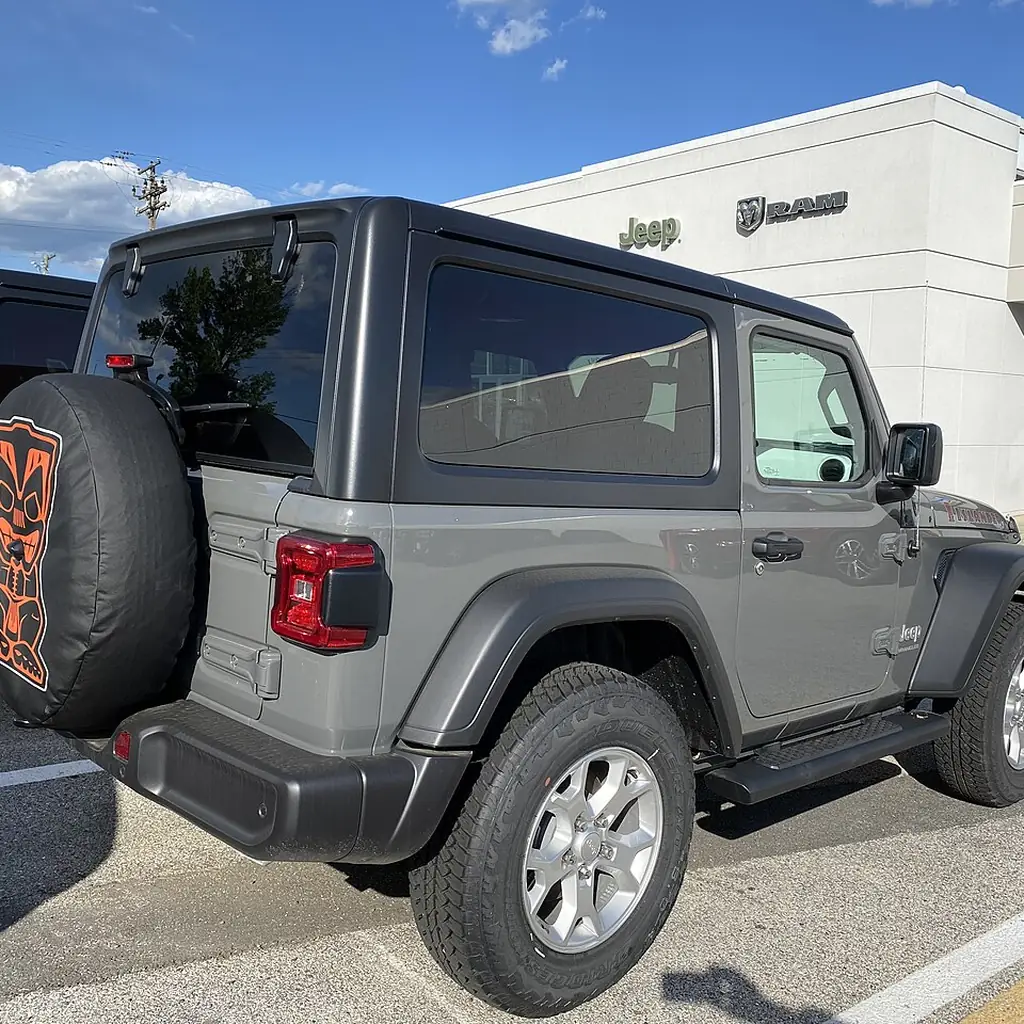 Rear three-quarter view of a 2021 Jeep Wrangler Islander with its spare tire on the swing gate.