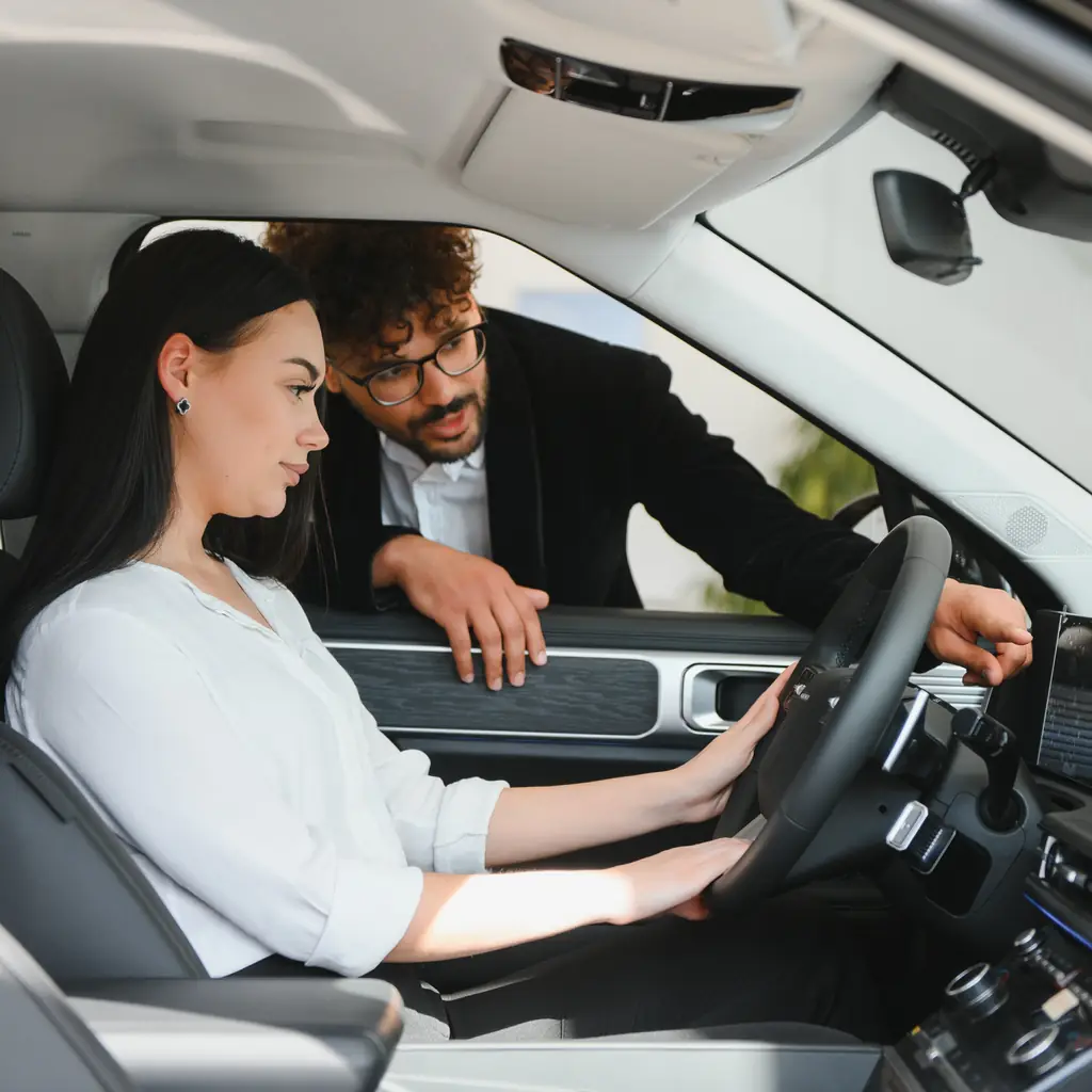 An adviser explains dashboard controls to a seated driver.