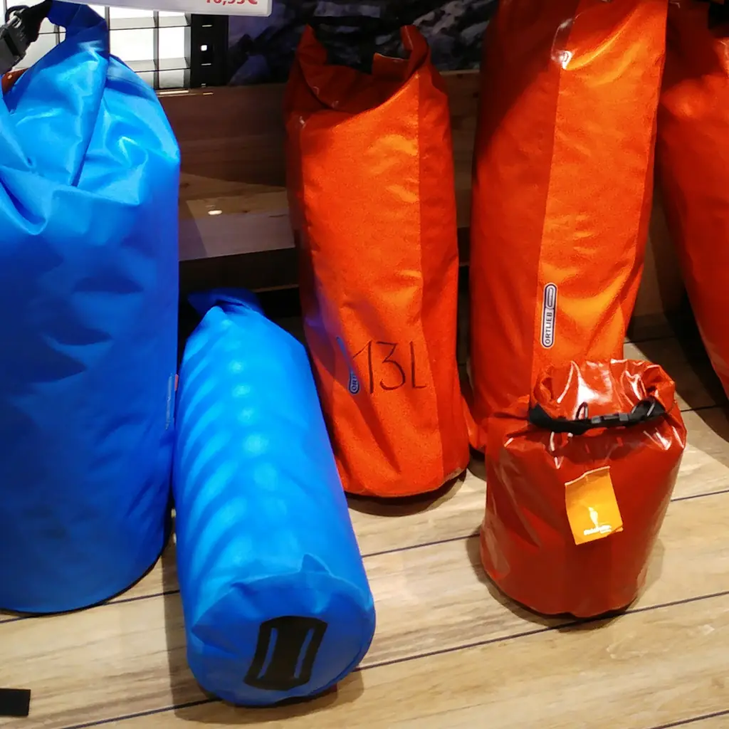 Blue and orange waterproof dry bags displayed with their roll-top closures.